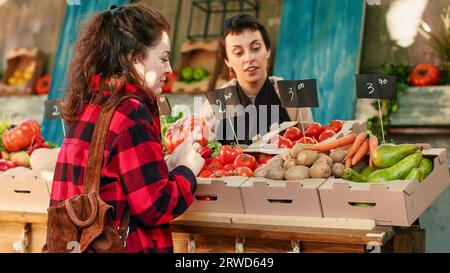 Client féminin achetant des produits naturels bio du vendeur au stand greenmarket, choisissant des fruits et légumes écologiques biologiques pour une alimentation saine. Propriétaire d'une entreprise vendant des produits locaux. Prise de vue à main levée. Banque D'Images