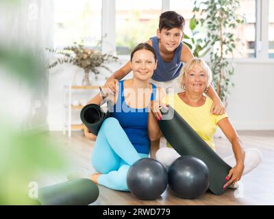 Trois personnes d'âges différents engagées dans le yoga assis sur le sol dans la salle de formation Banque D'Images