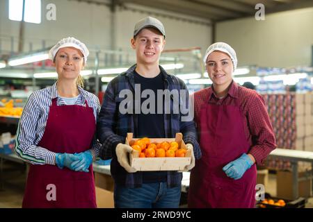 Travailleurs d'usine de tri positif de fruits debout avec des tangerines sélectionnées Banque D'Images