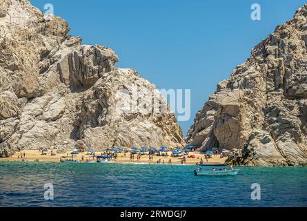 Mexique, Cabo San Lucas - 16 juillet 2023 : étroite parcelle de sable entre des falaises rocheuses menant de l'autre côté, la Playa de los Amantes. Parapluies bleus et su Banque D'Images