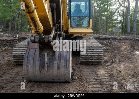 Gros plan du godet et des chenilles d'une excavatrice sur le sol près des arbres, dans un nouveau chantier de construction de maison. Banque D'Images