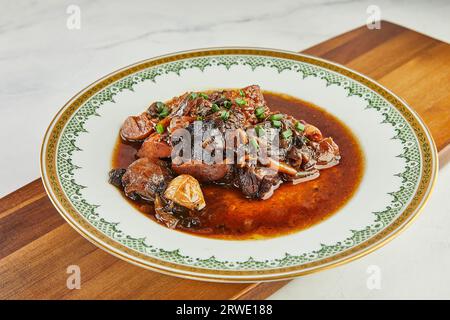 Ossobuco avec de l'ail et des oignons verts dans le vin rouge sur une assiette avec un ornement Banque D'Images