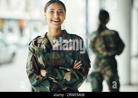 Portrait, soldat et femme les bras croisés, militaire et de sécurité avec le sourire, la confiance et la puissance. Visage, personne et guerrier avec fierté Banque D'Images