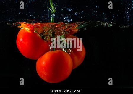 Tomate rouge fraîche tombant dans l'eau avec des éclaboussures d'eau et des bulles d'air isolées sur fond noir. Banque D'Images