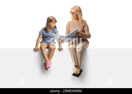 Femme et petite fille assises sur un panneau blanc et lisant un livre isolé sur fond blanc Banque D'Images