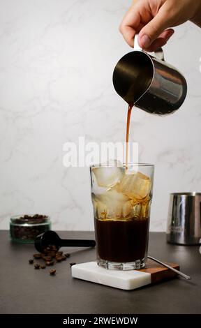 Verser le café dans un grand verre froid avec des glaçons, fond de marbre gris Banque D'Images