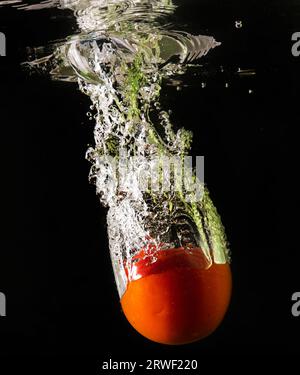 Tomate mûre tombe profondément sous l'eau avec un grand bruit. Banque D'Images