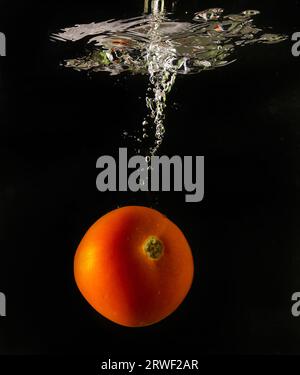 Tomate mûre tombe profondément sous l'eau avec un grand bruit. Banque D'Images