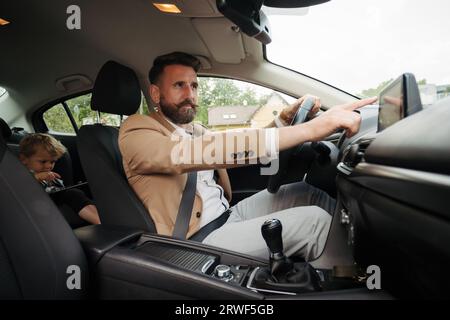 Jeune homme d'affaires touchant l'écran tactile multimédia dans la voiture. Banque D'Images