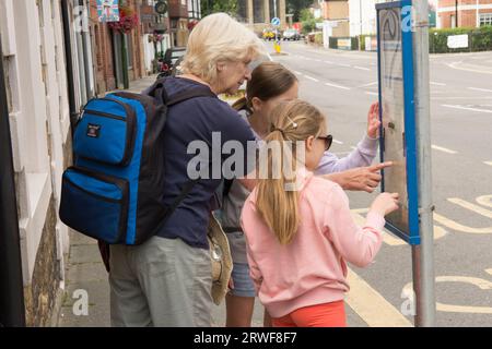 jeunes filles avec grand-mère debout à un arrêt de bus essayant de travailler sur l'horaire ou l'horaire, les transports publics Banque D'Images