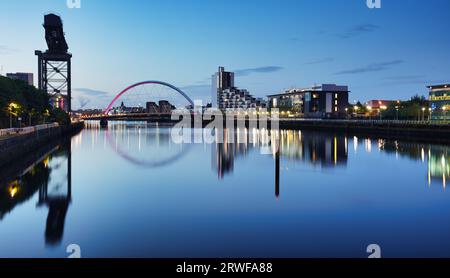 Magnifique Sunset Clyde Arc Bridge de l'autre côté de la rivière à Glasgow, Écosse, Royaume-Uni. Il fait beau temps avec réflexion sur l'eau, le ciel bleu, les lumières des bâtiments Banque D'Images