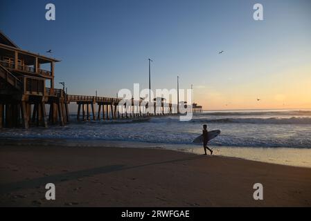 Un surfeur porte sa planche le long de la plage lors d'une matinée de surf au large de Jennette's Pier à Nags Head, en Caroline du Nord. Banque D'Images