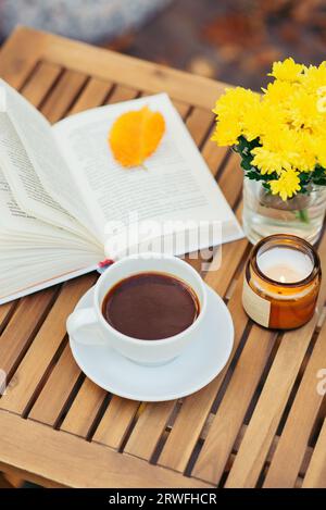 fleurs jaunes, tasse de boisson chaude et livre sur une table en bois en plein air. Nature morte d'automne Banque D'Images