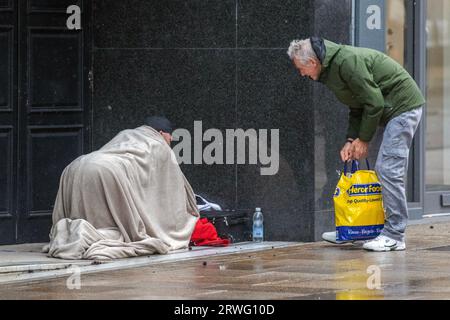 Homme donnant de la nourriture aux sans-abri à Preston, Lancashire. UK Météo sept. 2023. Magasins, acheteurs shopping sur une journée venteuse avec de fortes averses à Preston. Restant venteux, avec des gales localement à l'ouest. Des épisodes de pluie lourde et persistante sont attendus cet après-midi. Crédit. MediaWorldImages/AlamyLiveNews Banque D'Images