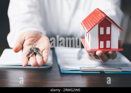 Clé de maison en main, clé avec maison modèle sur la table en bois, concept d'économie d'argent, investissement immobilier, prêt immobilier, hypothèque inversée, pile d'argent de pièces d'or Banque D'Images