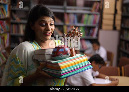 Enseignante indienne tenant une liasse de livres dans ses mains, debout dans la bibliothèque, étudiant la pression, la force éducative. Banque D'Images