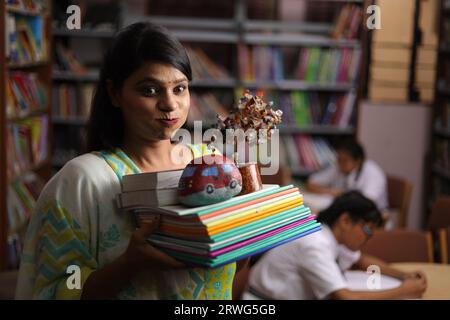 Enseignante indienne tenant une liasse de livres dans ses mains, debout dans la bibliothèque, étudiant la pression, la force éducative. Banque D'Images