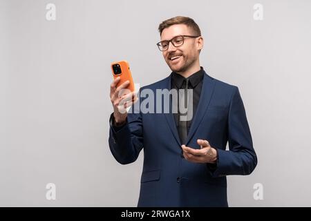 Homme d'affaires souriant confiant ayant une conversation en ligne sur smartphone sur fond gris. Banque D'Images