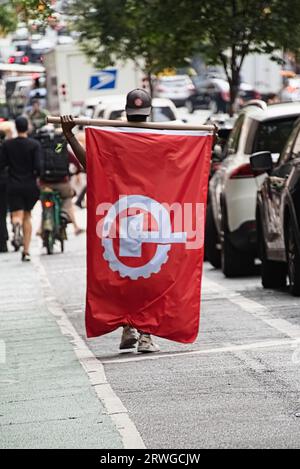 New York, NY - 17 septembre 2023 : drapeau du Parti communiste américain sur le dos d'un partisan noir afro-américain dans la rue de New York. Banque D'Images