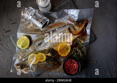 Poisson de bar frais. Poisson de bar cru avec des ingrédients d'épices et d'herbes pour la cuisson sur fond de pierre noire. Vue de dessus. Banque D'Images