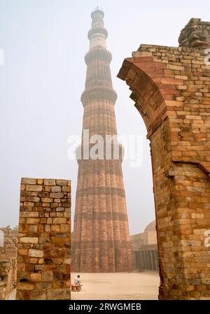 Qutb Minar le matin brumeux vu de l'intérieur des jardins historiques et des ruines flanquées d'arbres à Delhi, Inida. Banque D'Images