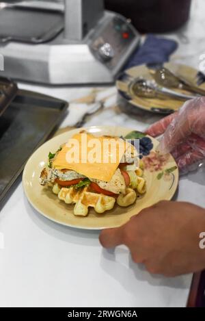 Chef tenant des gaufres belges fraîches avec poulet, fromage et tomate sur l'assiette Banque D'Images