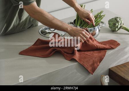 Asperges dans un pot plat inoxydable, hommes tenant une serviette en lin. Fond d'ingrédients de cuisson d'aliments sains avec des légumes frais Banque D'Images