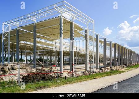 Grande structure de cadre en acier d'entrepôt inachevée sur des supports en béton armé avec toit en acier ondulé, fond de ciel bleu Banque D'Images