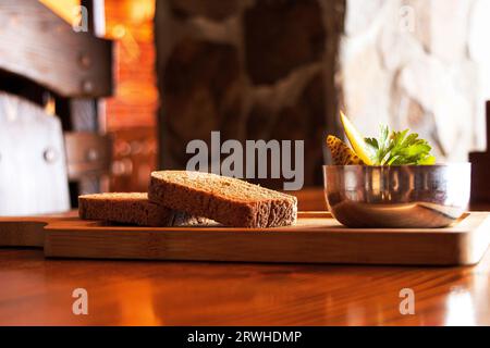 Deux morceaux de pain noir tranché et des cornichons dans un bol comme collation reposent sur une planche de bois sur une table sous le soleil, du pain sur la table Banque D'Images