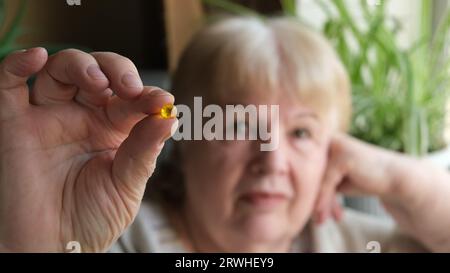 Femme âgée tenant la capsule jaune de gel oméga 3. Supplément d'huile de poisson Banque D'Images