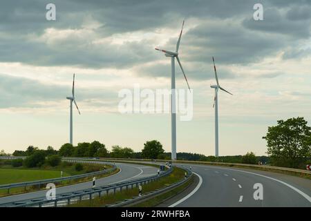 Les éoliennes se dressent le long de la route sur fond de nuages. Production d'énergie écologique verte. Banque D'Images