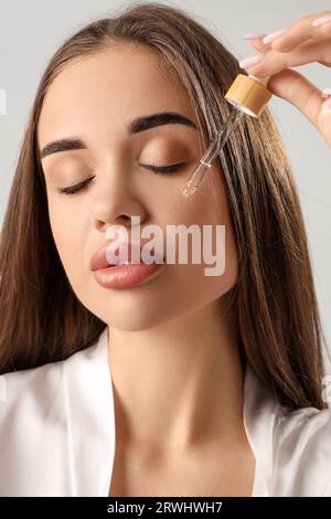 Jeune femme appliquant du sérum naturel sur son visage sur fond clair Banque D'Images