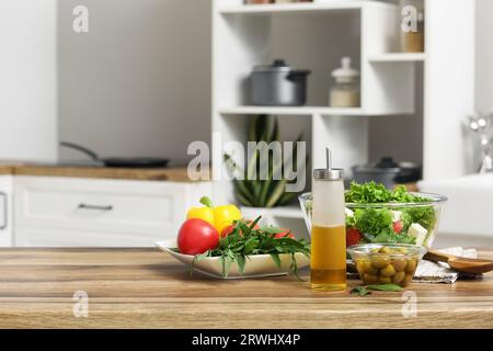 Bouteille avec huile, salade fraîche, olives et légumes sur table dans la cuisine Banque D'Images