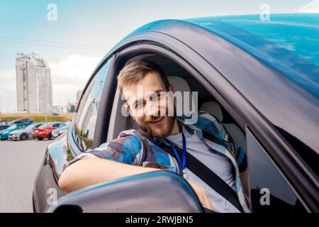 Instructeur masculin souriant assis sur le siège passager et regardant par la fenêtre de la voiture. Test de conduite, cours de conducteur, concept d'examen Banque D'Images