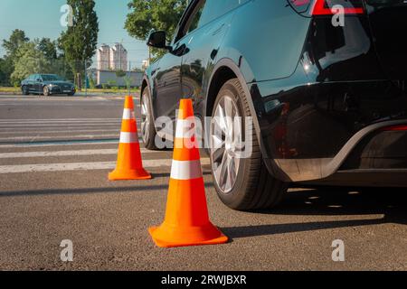 Cônes de signalisation près de voiture noire à l'extérieur. Voiture moderne sur piste d'essai. Test de conduite, cours de conducteur, concept d'examen Banque D'Images