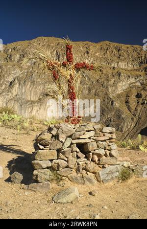 Croix chrétienne enroulé autour de fleurs sur le paysage aride du Pérou près de Canon del Colca Banque D'Images