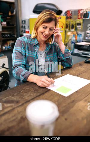 Portrait de jeune femme blonde souriante recevant l'ordre par téléphone pour boutique de commerce électronique Banque D'Images