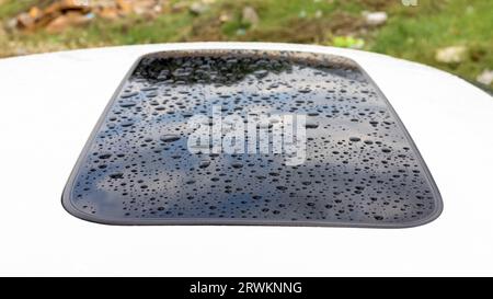 Gouttes de pluie sur le toit ouvrant d'une voiture blanche. Mise au point sélective et gros plan. Banque D'Images