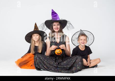 Halloween en famille. Une famille heureuse, une mère et des enfants en costumes de sorcier et sorcellerie créepy tenant un panier en forme de citrouille avec des friandises sur un b blanc Banque D'Images