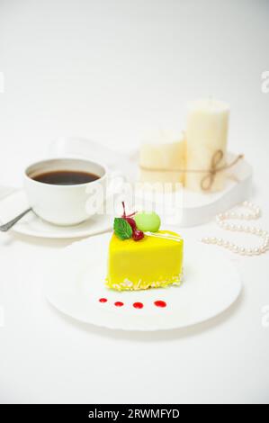 Une tasse de café avec un gâteau en forme de cœur dans un glaçage jaune sur une assiette sur un fond clair Banque D'Images