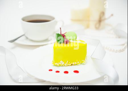 Une tasse de café avec un gâteau en forme de cœur dans un glaçage jaune sur une assiette sur un fond clair Banque D'Images