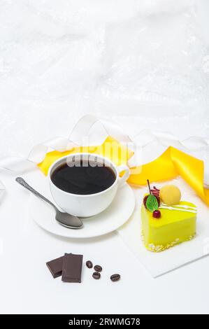 Une tasse de café avec un gâteau en forme de cœur dans un glaçage jaune sur une assiette sur un fond clair Banque D'Images