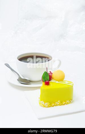 Une tasse de café avec un gâteau en forme de cœur dans un glaçage jaune sur une assiette sur un fond clair Banque D'Images