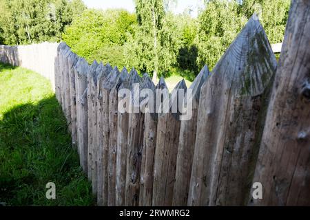 Gros plan d'un mur en bois fait de piquets en bois pointus sur une journée ensoleillée d'été. Ciel bleu clair avec des nuages occasionnels. Flou artistique. Protection, sécurité, Banque D'Images