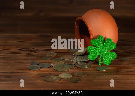 Concept de jour de St Patricks avec pot avec des pièces de monnaie anciennes dispersées et shamrock sur fond en bois vintage, gros plan. Banque D'Images