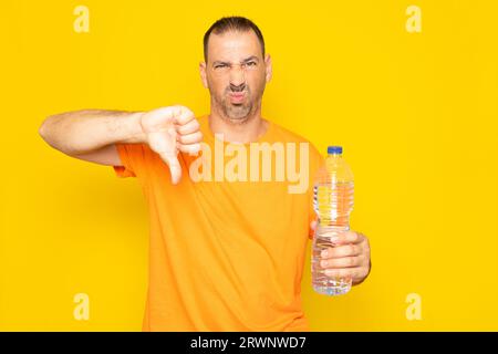 Homme hispanique avec barbe dans ses 40 ans faisant le geste de je n'aime pas avoir à acheter des bouteilles en plastique pour l'eau, isolé sur fond jaune Banque D'Images