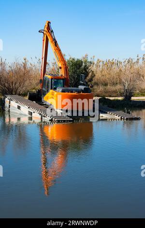 Excavatrice avec chenille sur la rive d'un canal ou d'un ruisseau enlevant la boue sous l'eau Banque D'Images