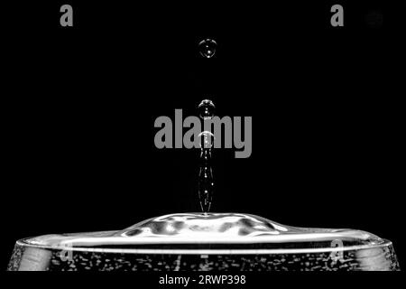 Gouttes d'eau réfléchissantes émergeant d'un verre d'eau devant un fond noir. Banque D'Images