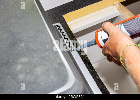Un homme applique un calfeutrage au silicone avec un pistolet sur le bord d'un évier de cuisine pour l'installer sur le comptoir. Banque D'Images