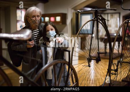 Tween écolière et femme âgée tuteur dans des masques de visage regardant vélo d'époque dans le musée Banque D'Images